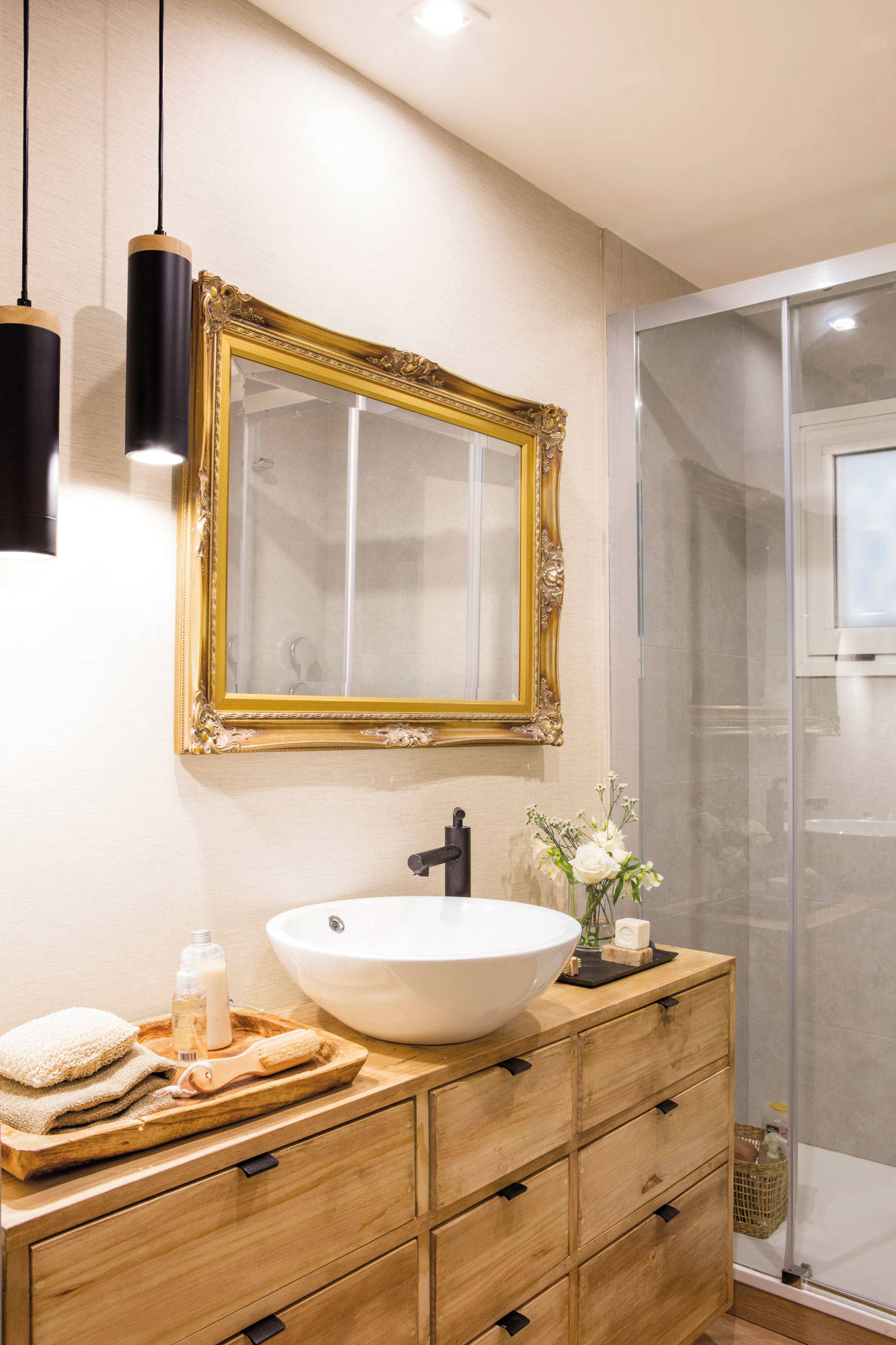 Baño con mueble de madera, espejo con marco dorado y lámparas de suspensión negras