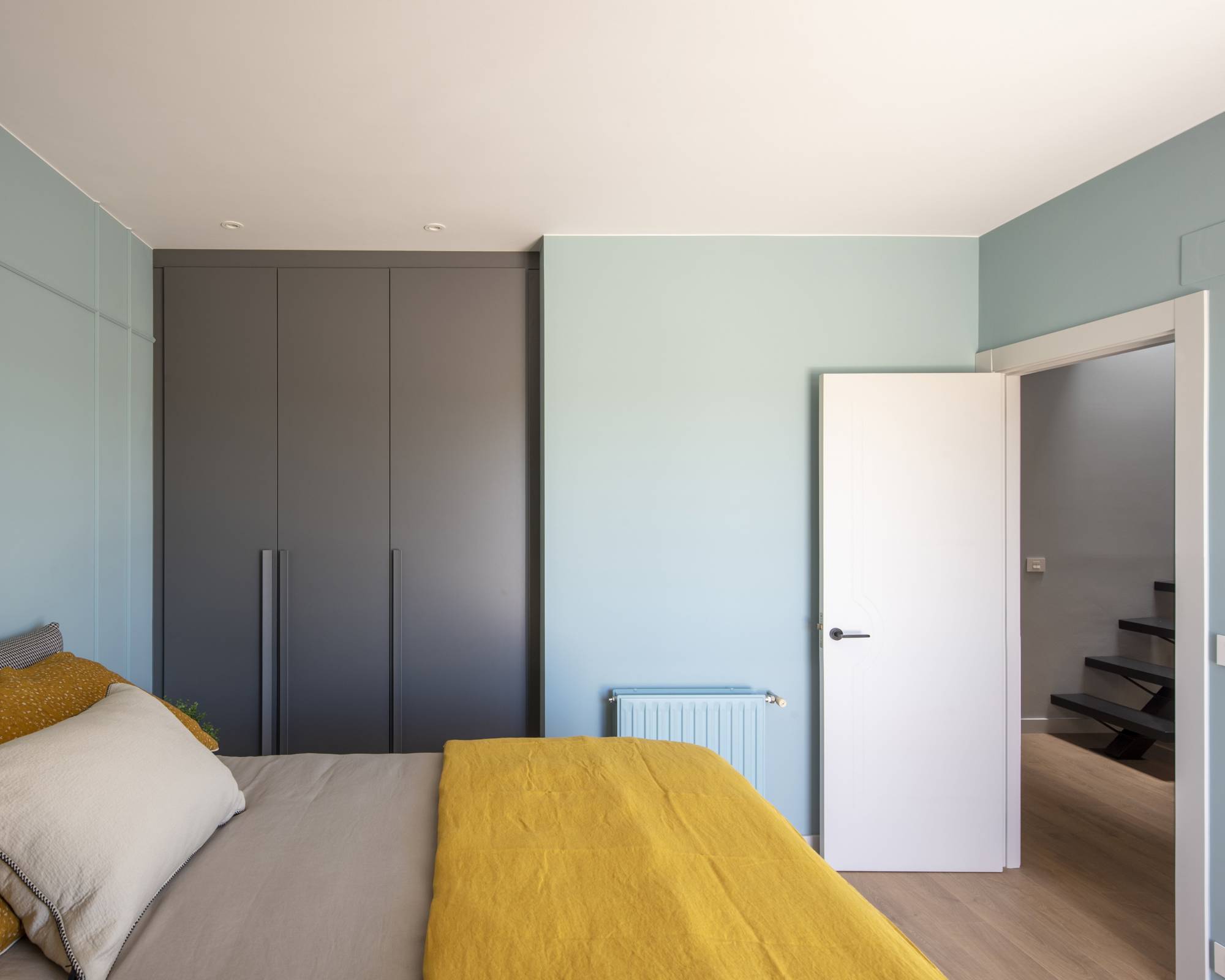 Dormitorio principal después de la reforma con paredes azules y ropa de cama mostaza. 
