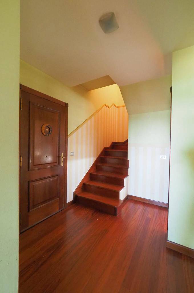Entrada con suelos de madera, escalera y paredes verdes antes de la reforma.
