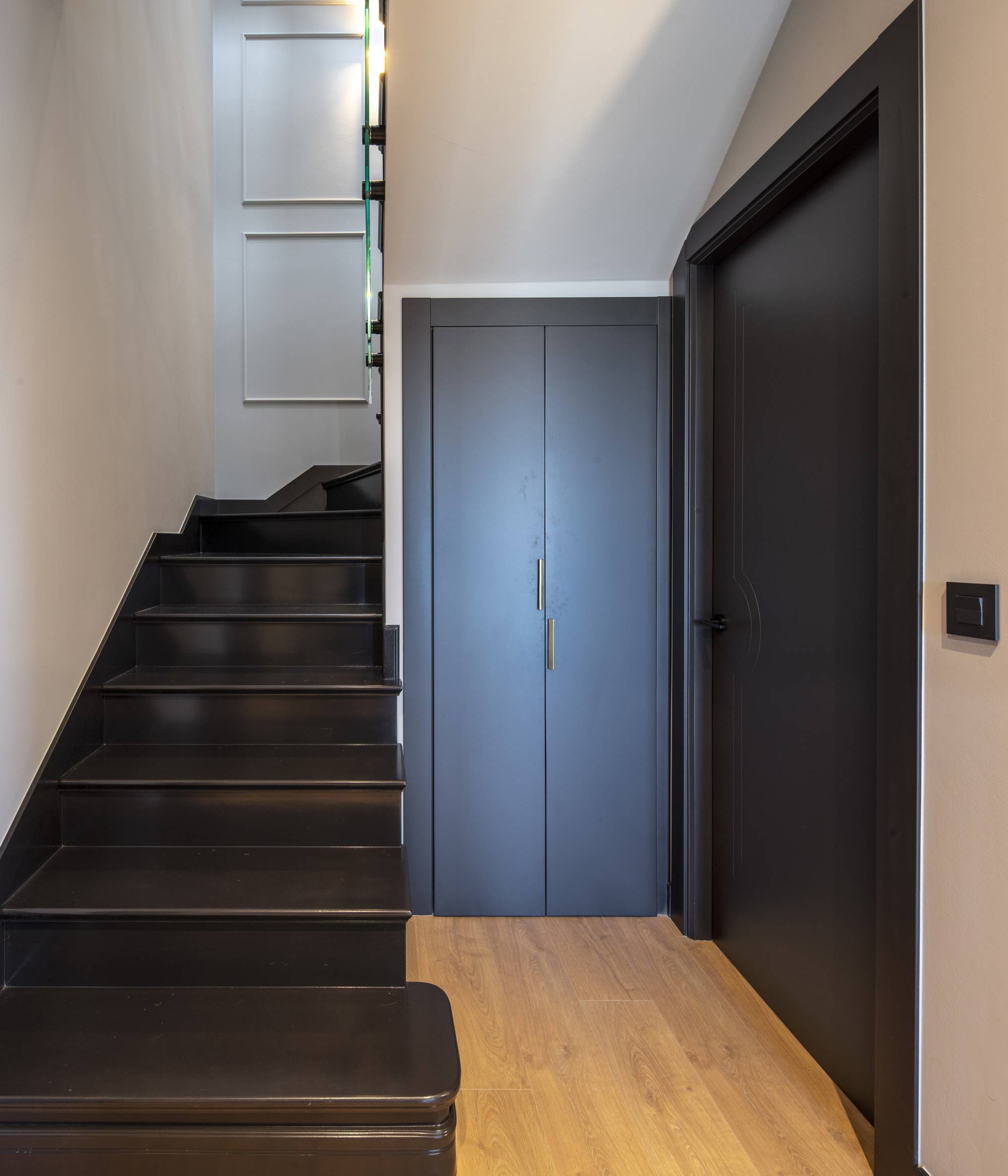 Entrada moderna con escaleras oscuras, armario, y suelo de madera.