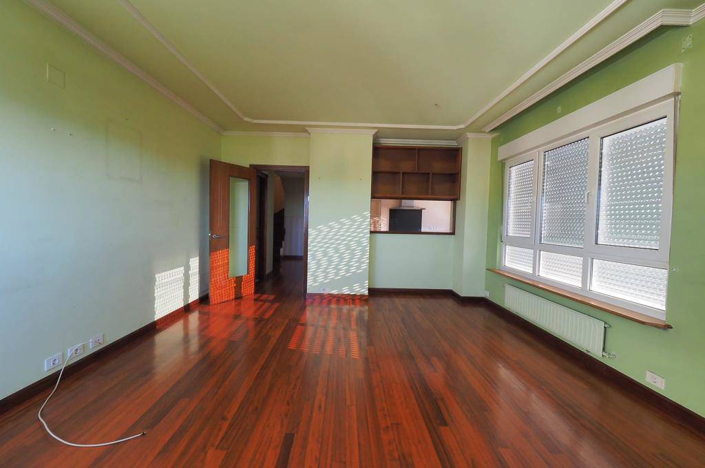 Sala de estar antes de la reforma con suelo de madera oscuro y paredes verdes.