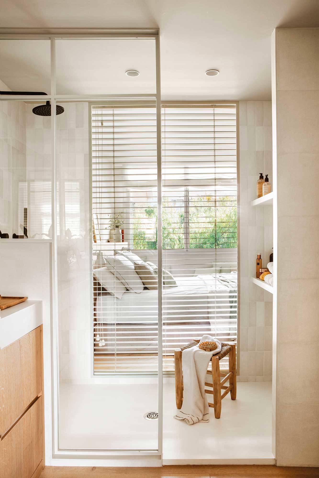 Baño pequeño con pared acristalada de la ducha que comunica con el dormitorio