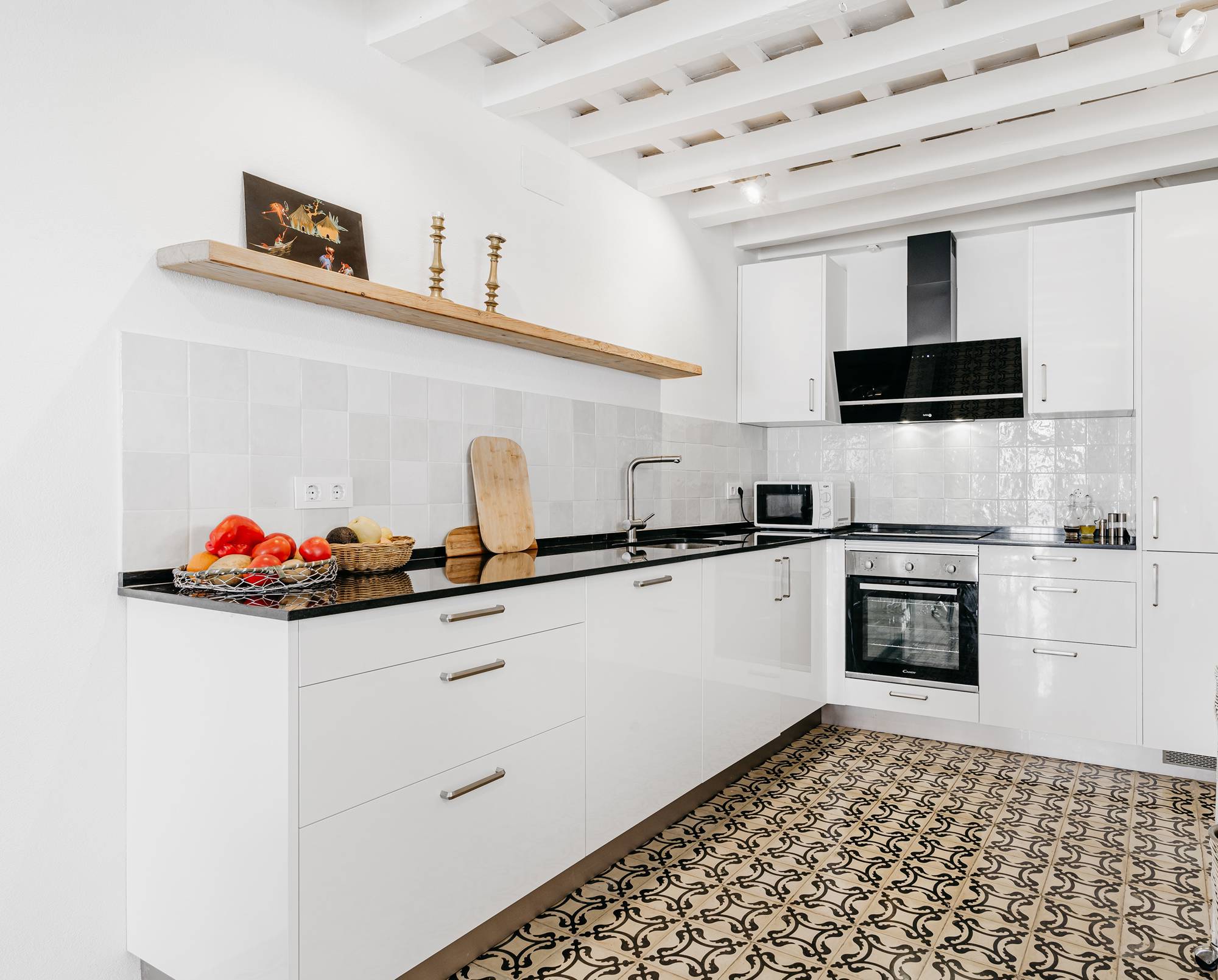 Una cocina moderna con muebles blancos, vigas en el techo y baldosas hidráulicas en el suelo.