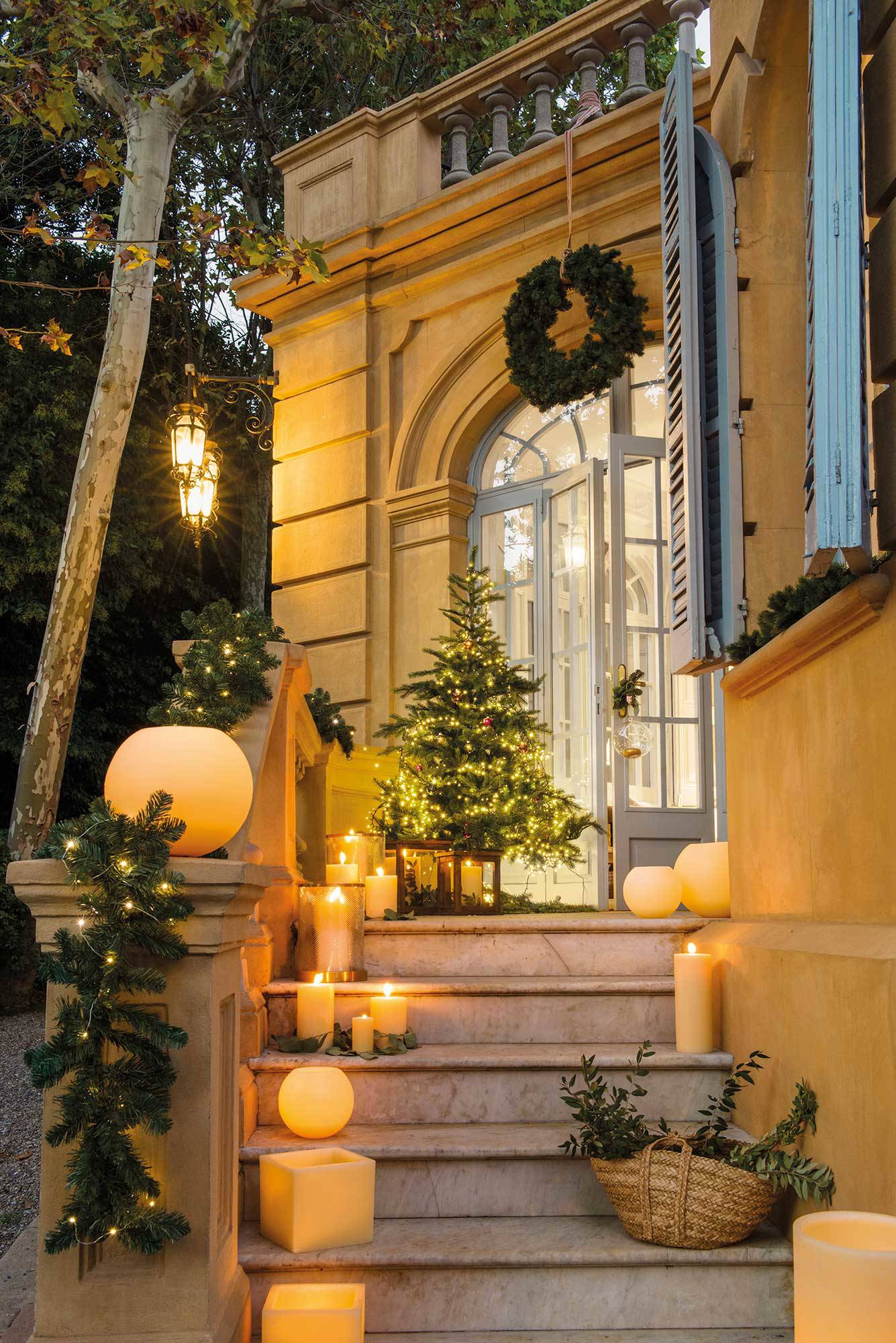 Exterior de casa decorada de Navidad con árbol y velas.