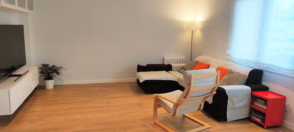 Salón moderno con mueble blanco, sofá negro y suelo de madera