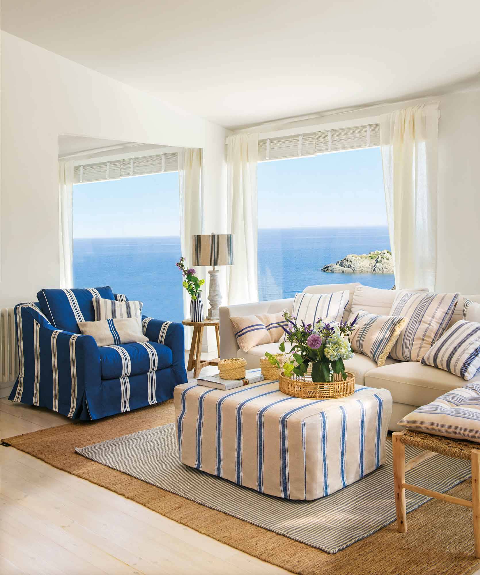 Salón con vistas al mar con butaca con funda azul con rayas blancas. 