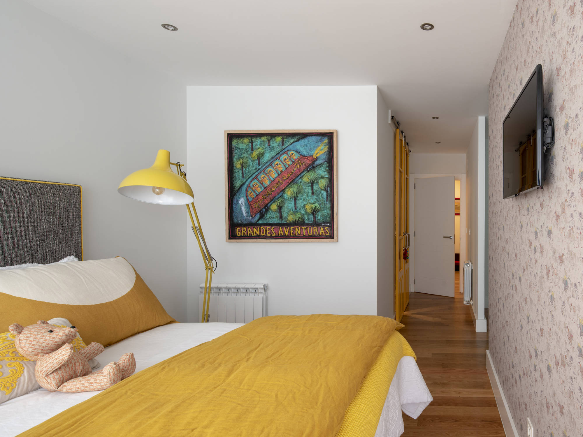Dormitorio principal después de la reforma con papel pintado, ropa de cama amarilla y baño propio.