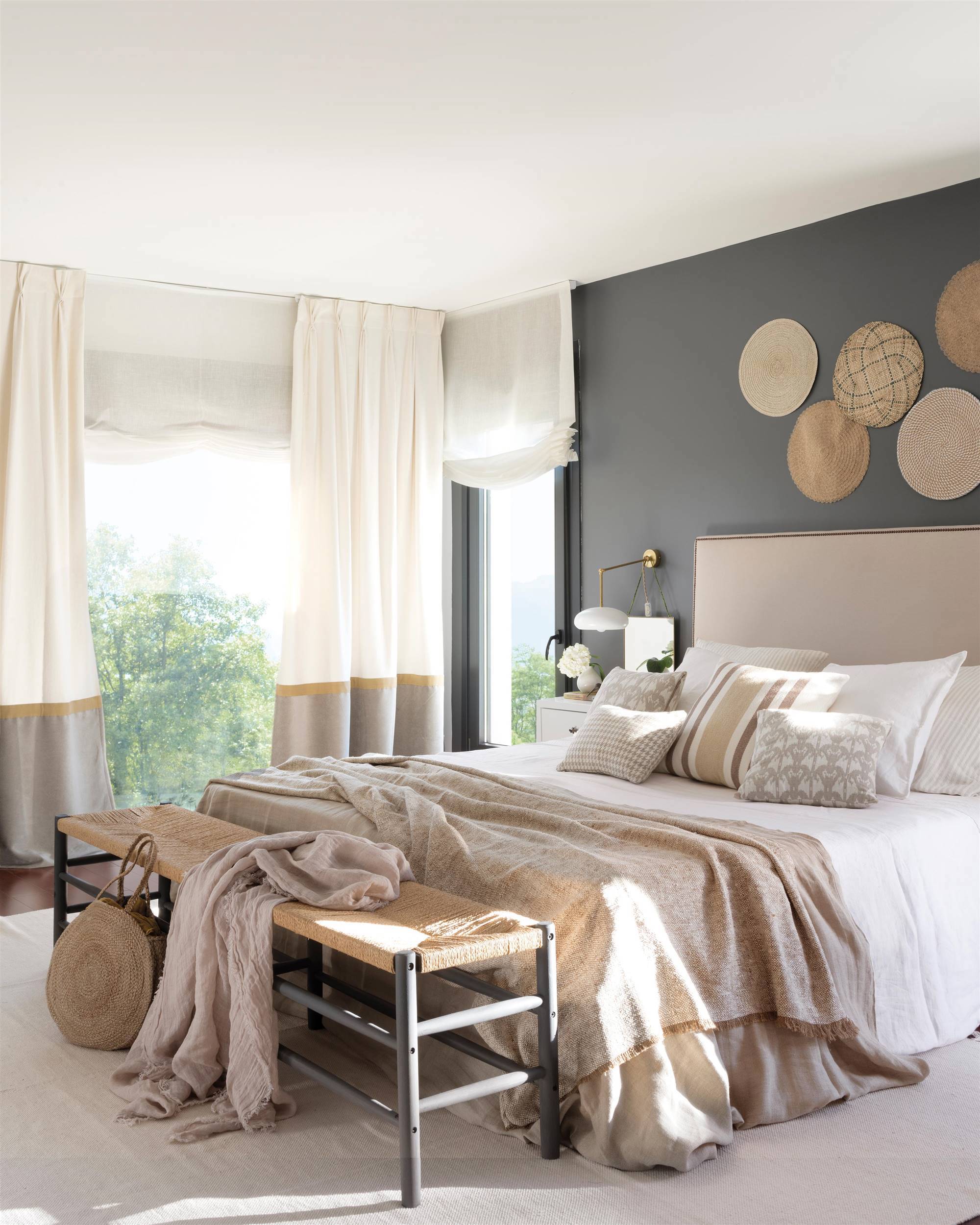 Dormitorio con pared gris, cabecero tapizado y banco de fibra.