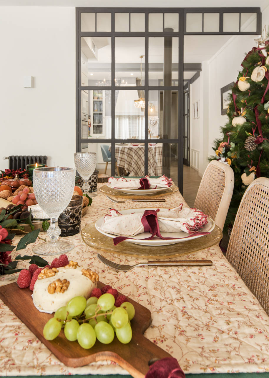Comedor con mesa navideña decorada de Navidad con vajilla de vidrio, textiles y tablas de madera.