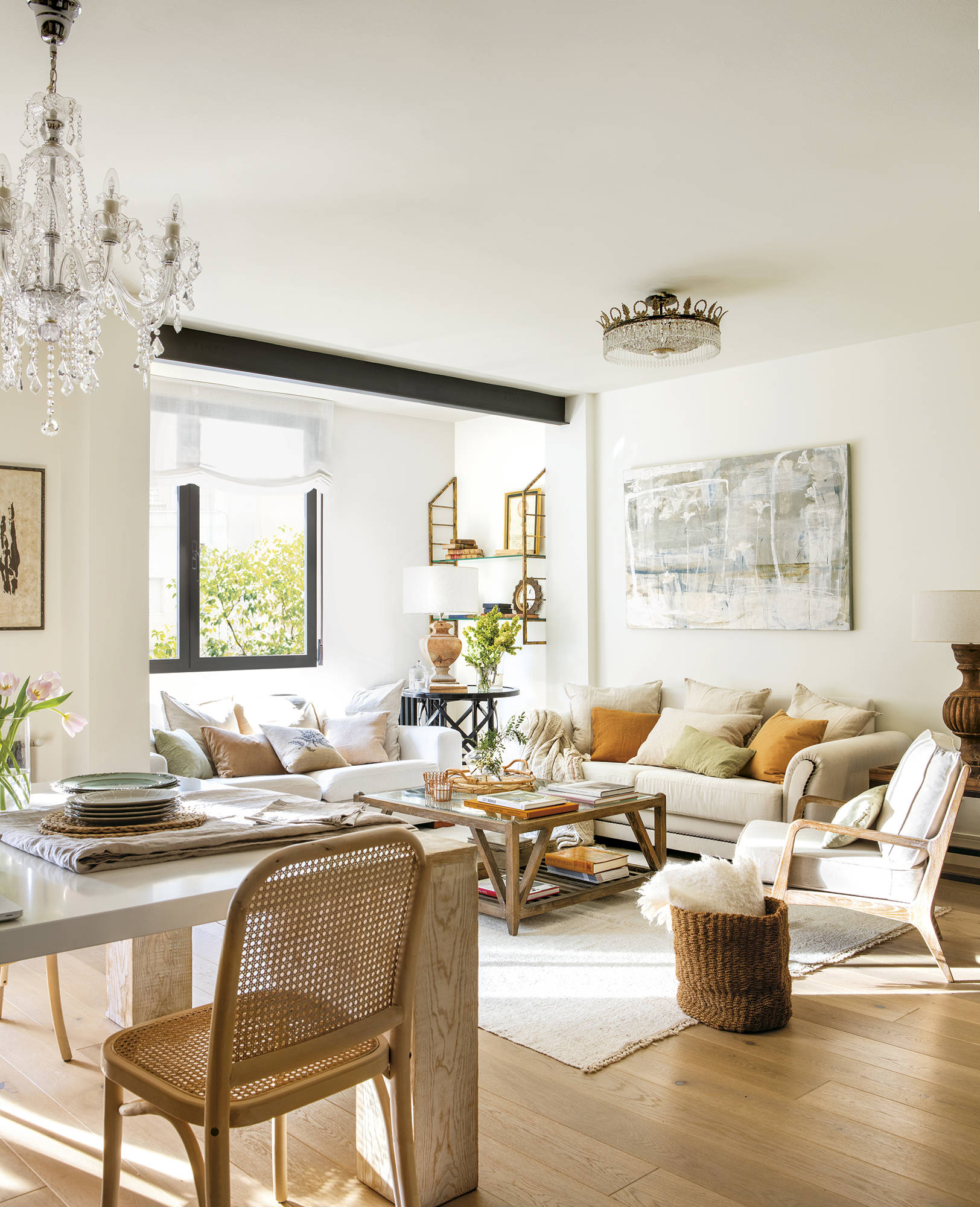 Salón y comedor en tonos claros con mesa de centro de madera, sillas de fibras, sofá beige y lámpara de araña.