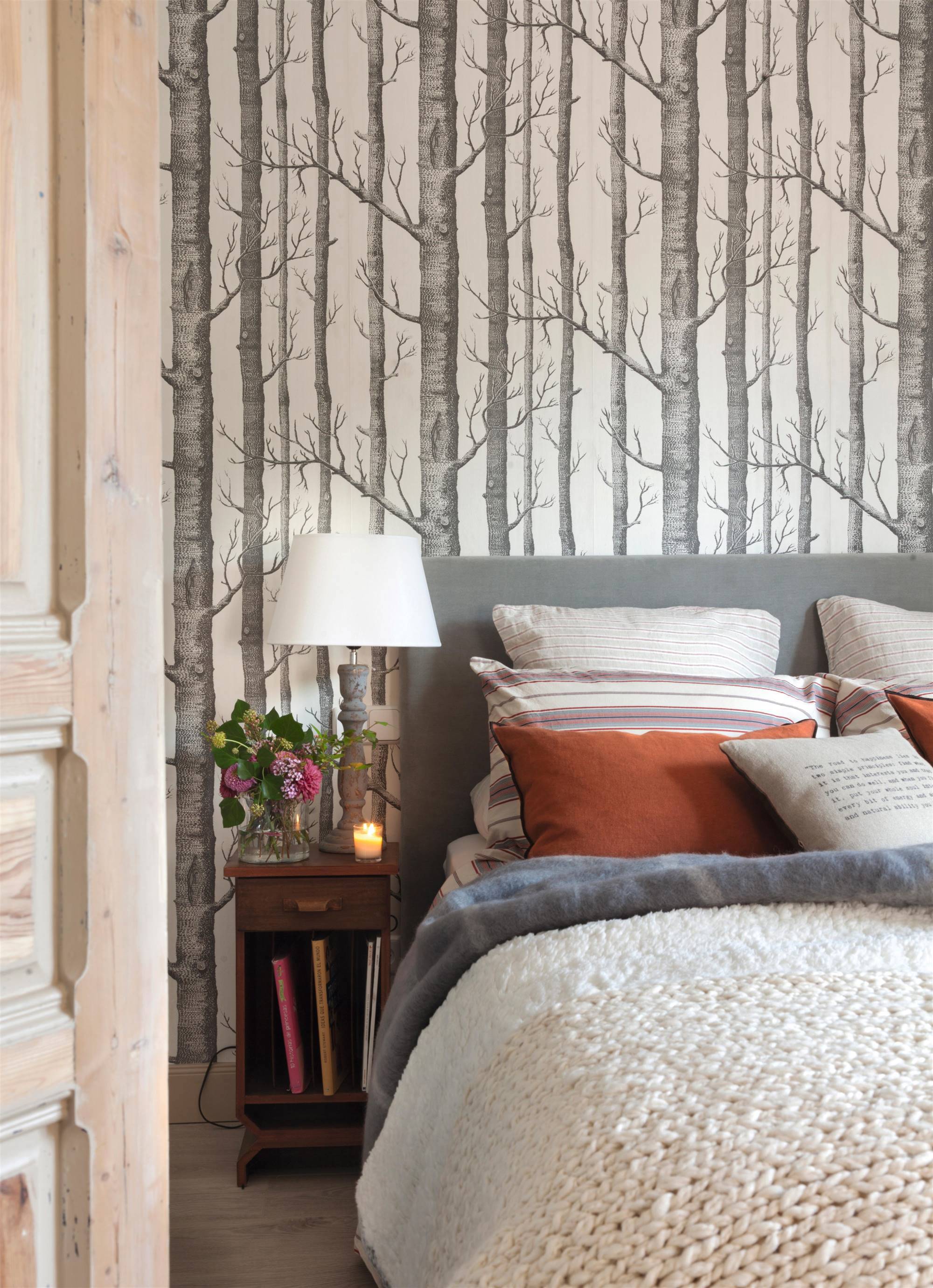 Dormitorio de invierno con papel pintado estampado, cabecero tapizado y manta de punto.