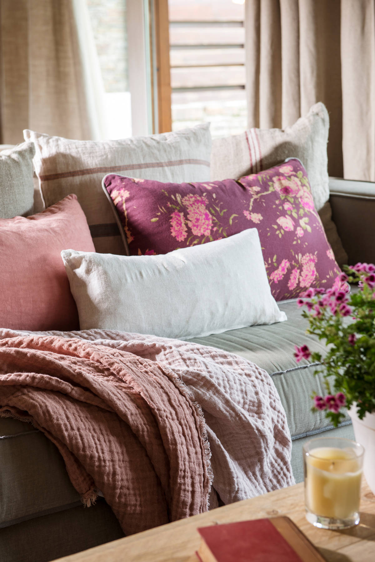 Cojines con flores en color granate y plaid en sofá claro.