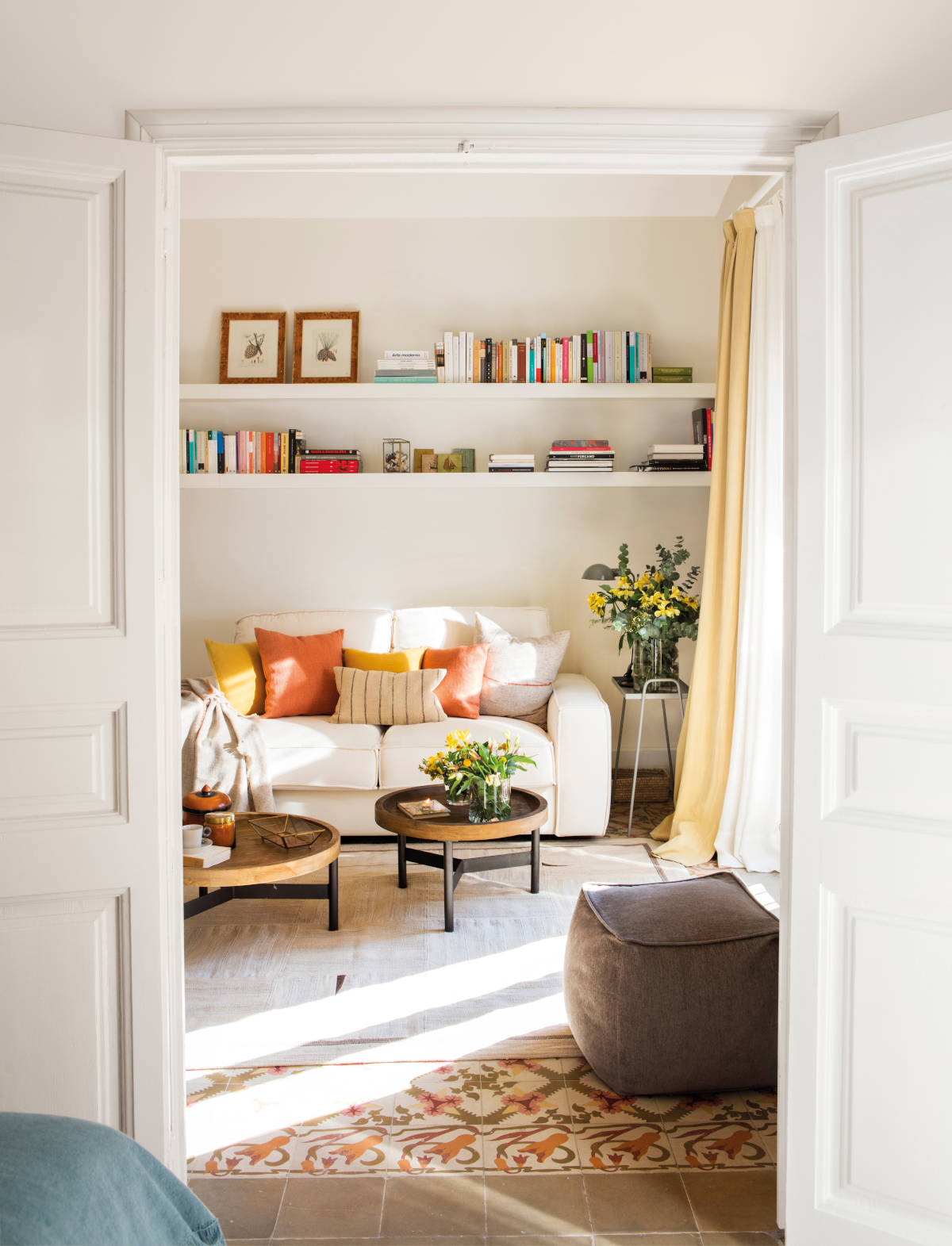 Salón con sofá cama blanco con mesas nido y estantería con libros. 