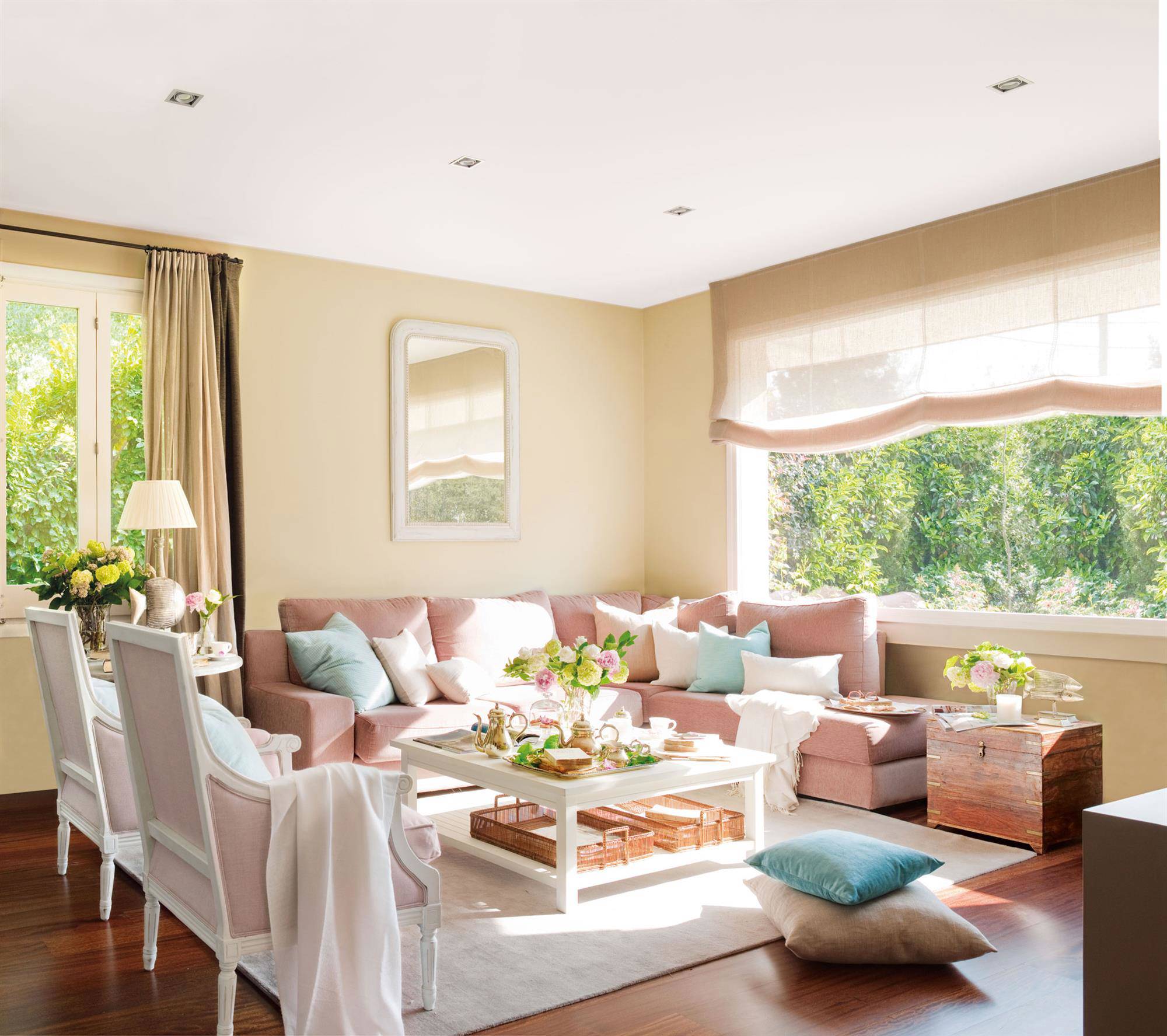 Salón con sofá modular rosa con butacas tapizadas en lino rosas y paredes beige.