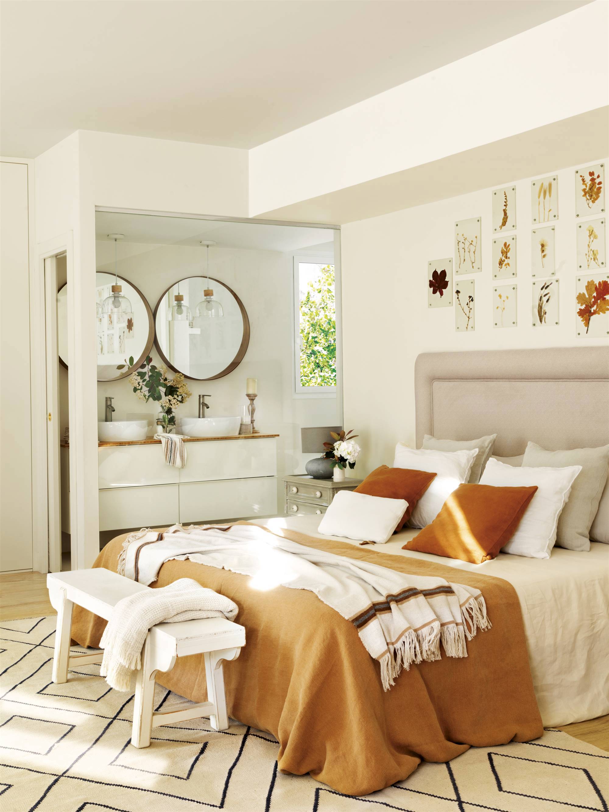 Dormitorio en suite con cabecero tapizado y ropa de cama ocre.