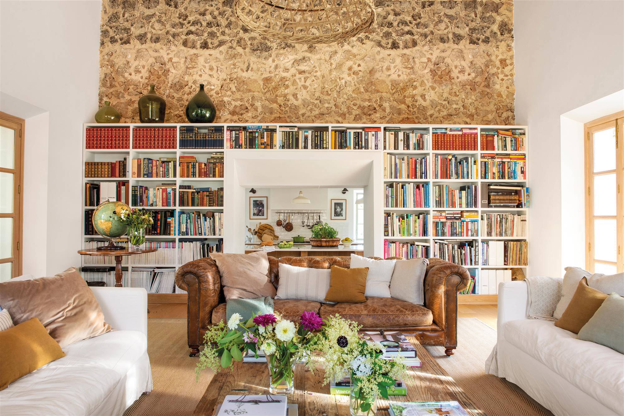 Salón rústico con pared de piedra con librería y sofá chéster de cuero. 