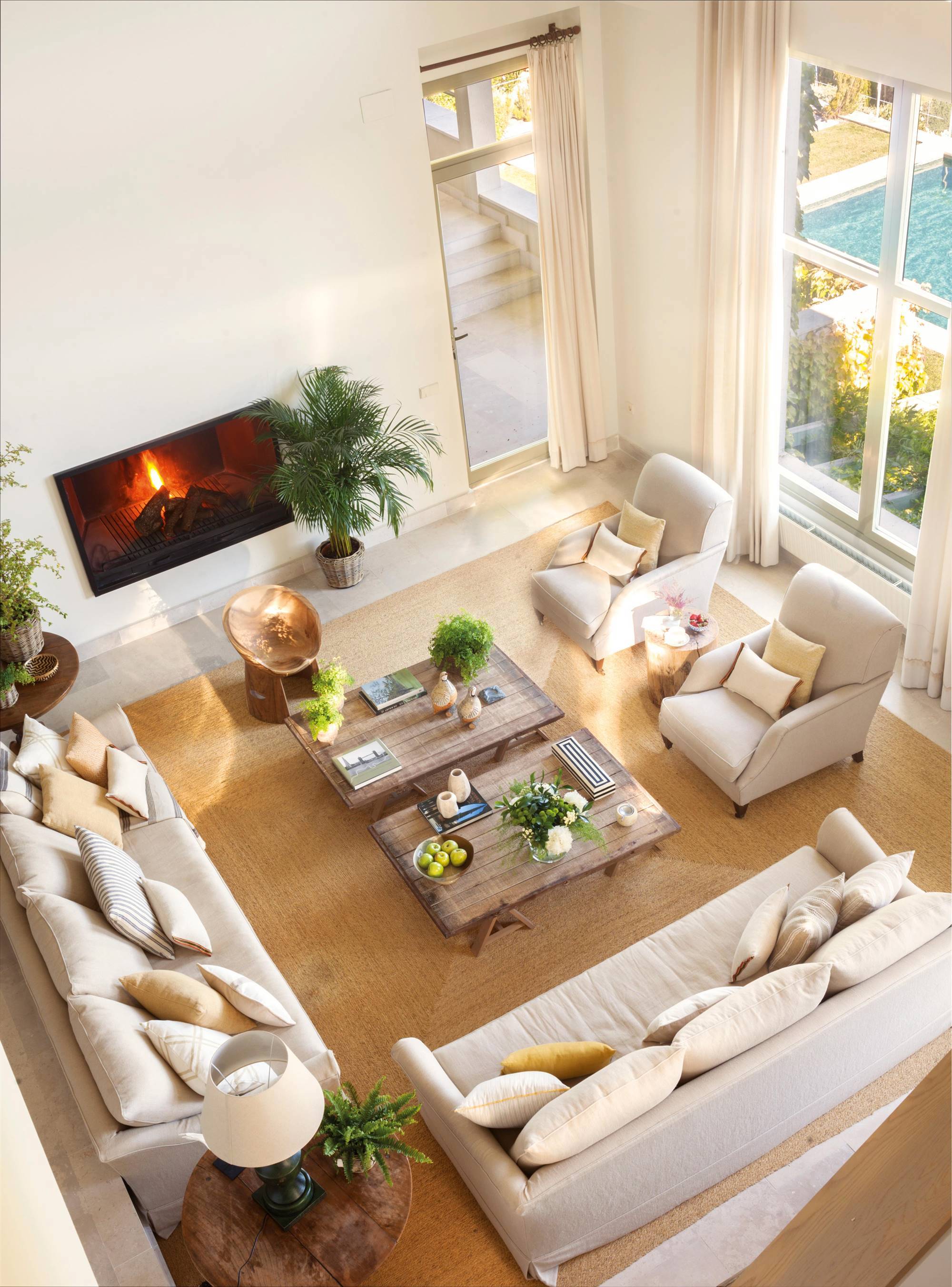 Vista cenital de salón con chimenea, sofás y butacas blancas y plantas.