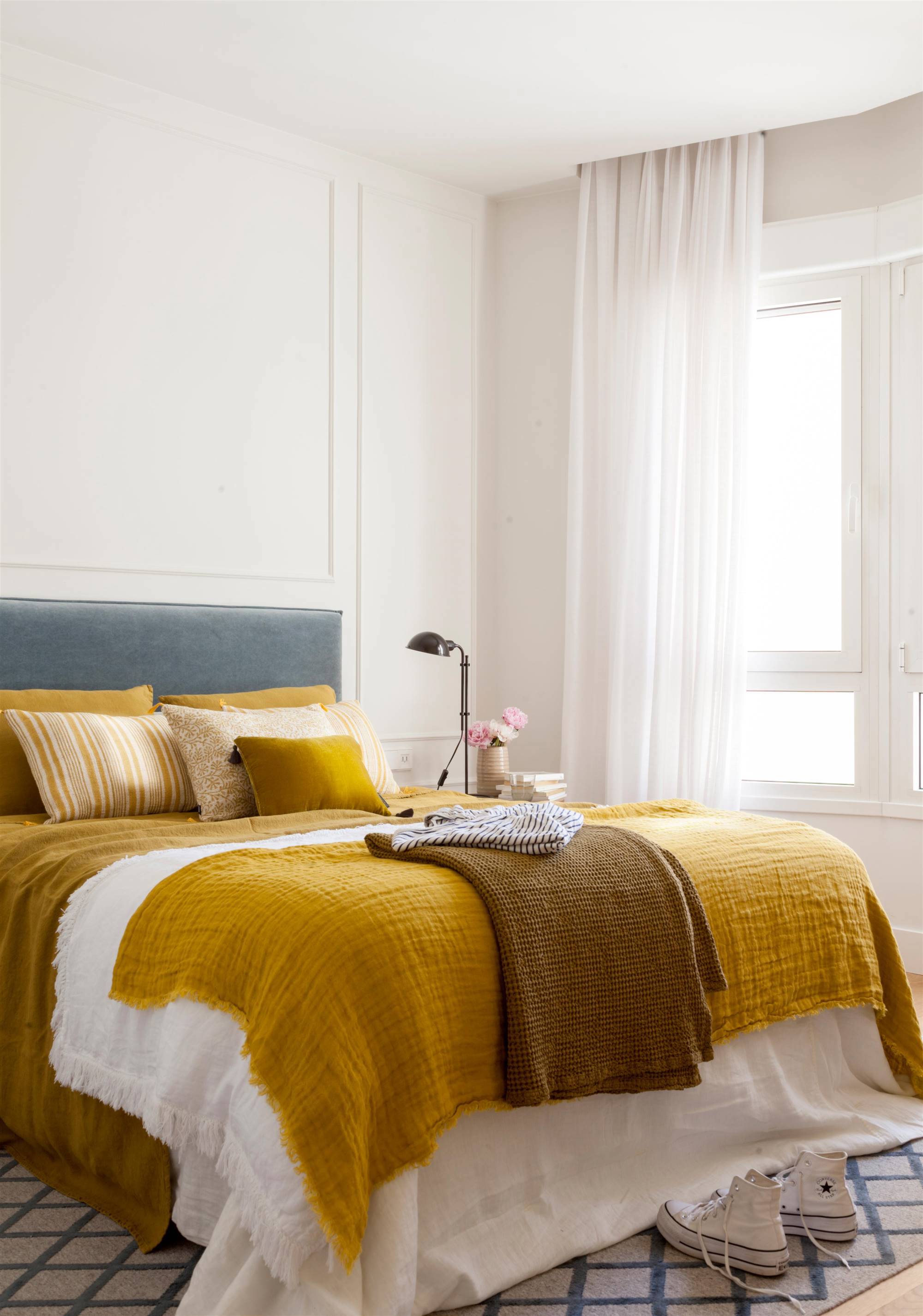 Dormitorio con paredes blancas, cabecero tapizado en terciopelo azul y ropa de cama mostaza