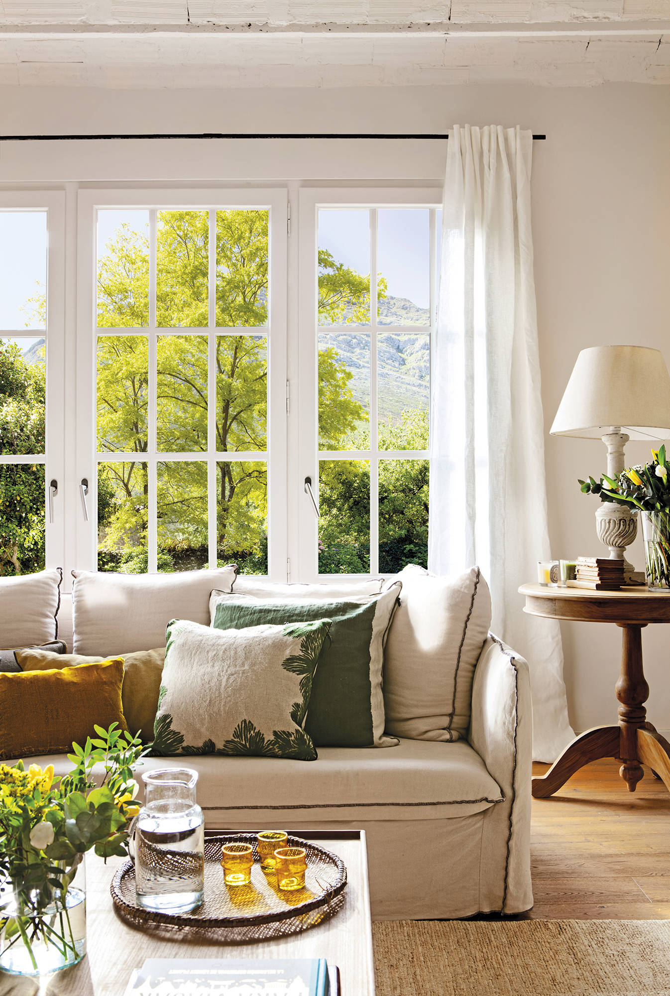 Detalle de sofá con poco fondo y reposabrazos fino delante de ventana con cuarterones.