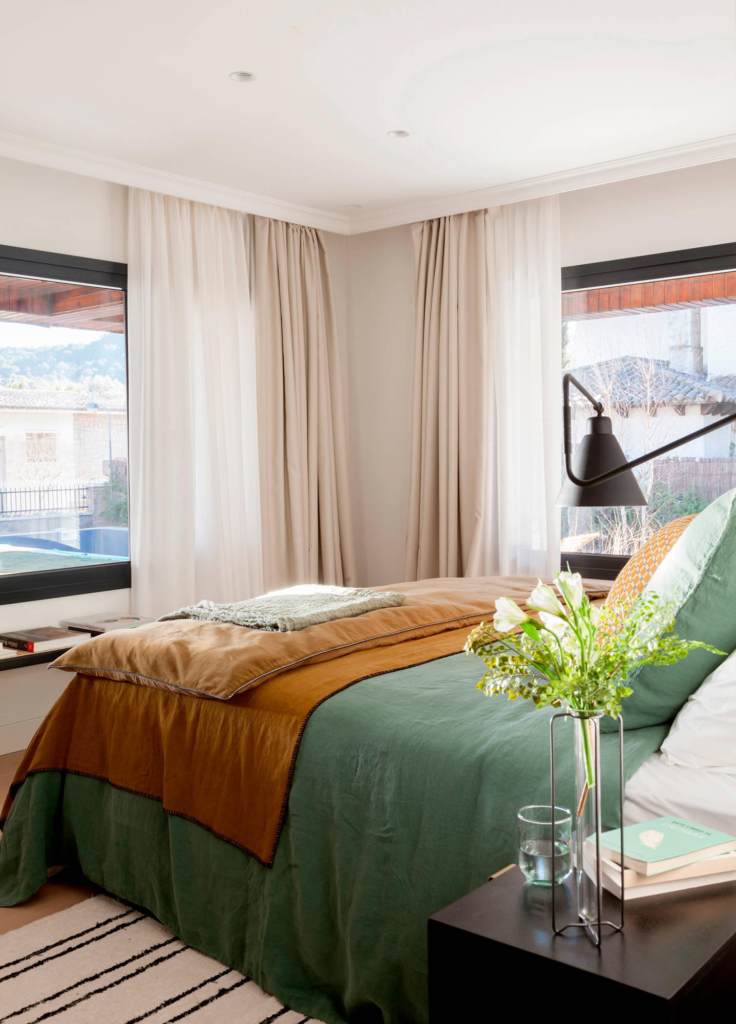 Dormitorio con cortinas dobles y topa de cama verde y marrón. 