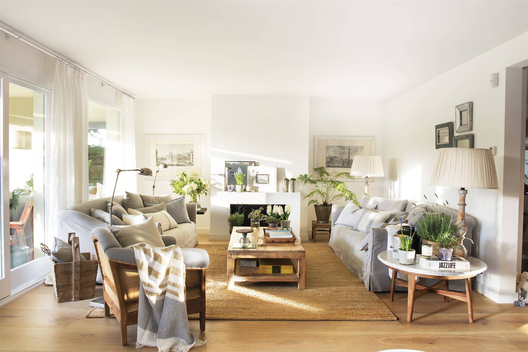 Salón nórdico con chimenea blanca, sofás y butaca de color gris, mesa de centro y auxiliar de madera y alfombra de fibras.