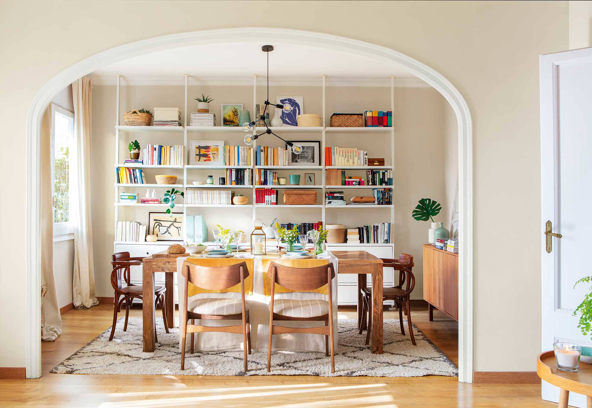 Comedor con arco, librería abierta, sillas diferentes y alfombra de diseño geométrico.