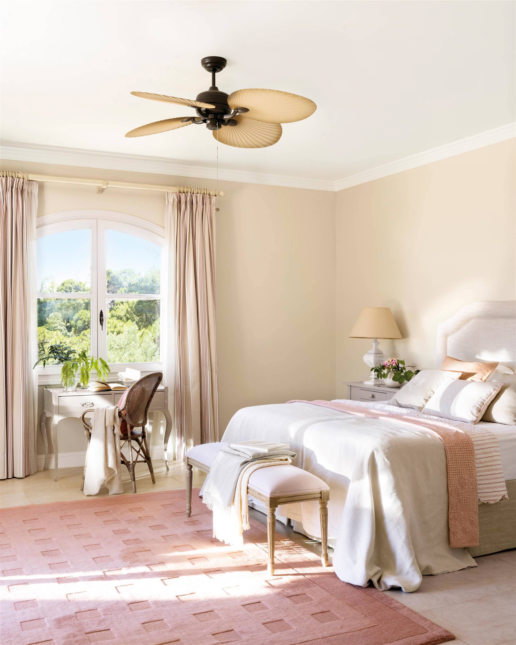Dormitorio con cabecero tapizado, lámpara ventilador y alfombra rosa.