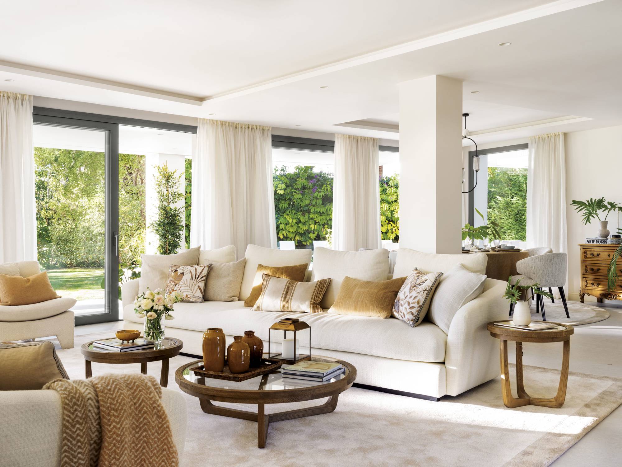 Salón blanco con sofás, mesas de centro de cristal y madera y cojines mostaza 00553576