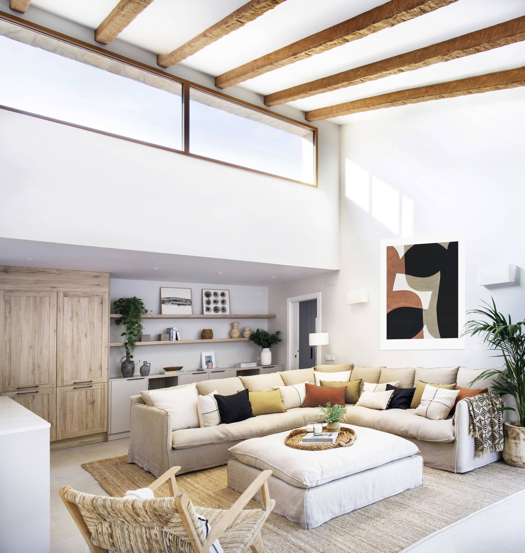Salón con sofá beige en forma de L, puff a juego, butaca y alfombra de fibras y vigas de madera en el techo.