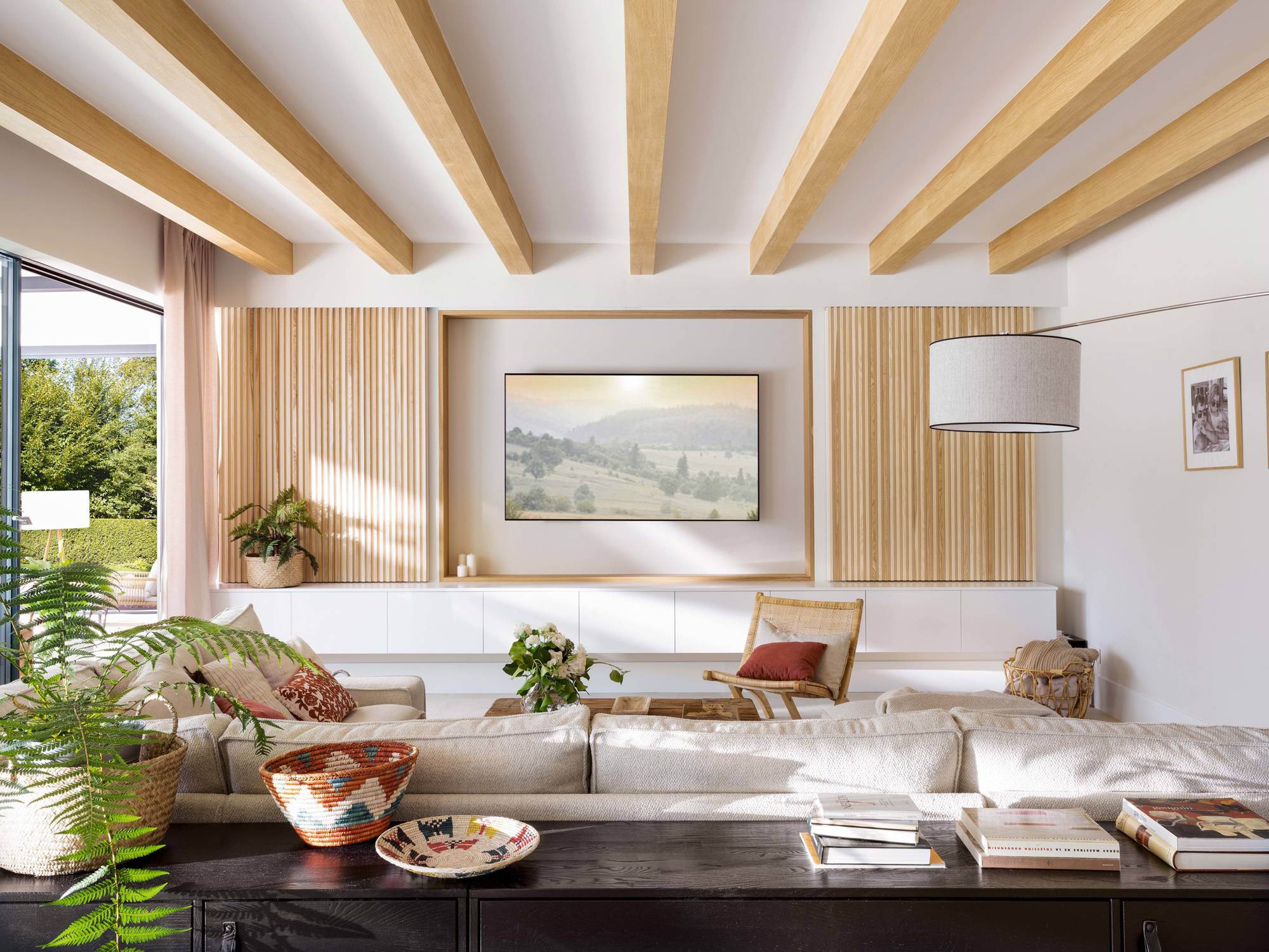 Salón con vigas de madera en el techo y mueble de palillería para ocultar la televisión.