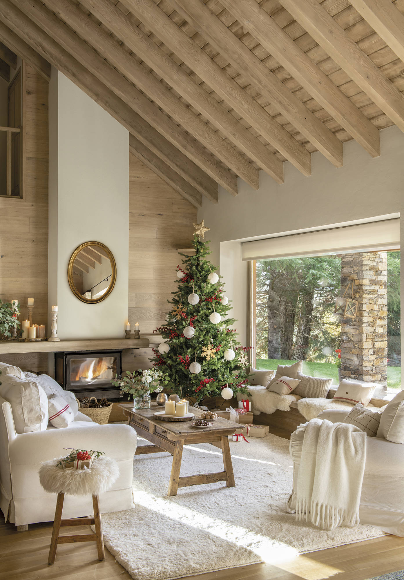 Salón rústico con vigas, sofás blancos, alfombra, chimenea y árbol de Navidad.