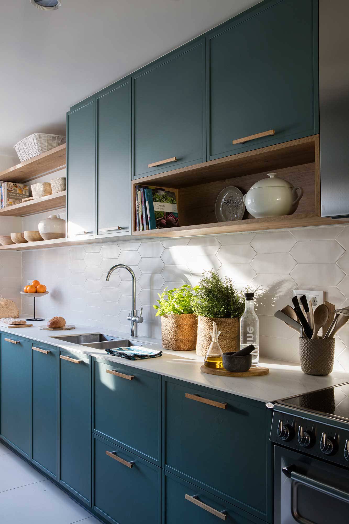 Cocina con muebles azul verdoso, azulejos blancos y detalles en madera.