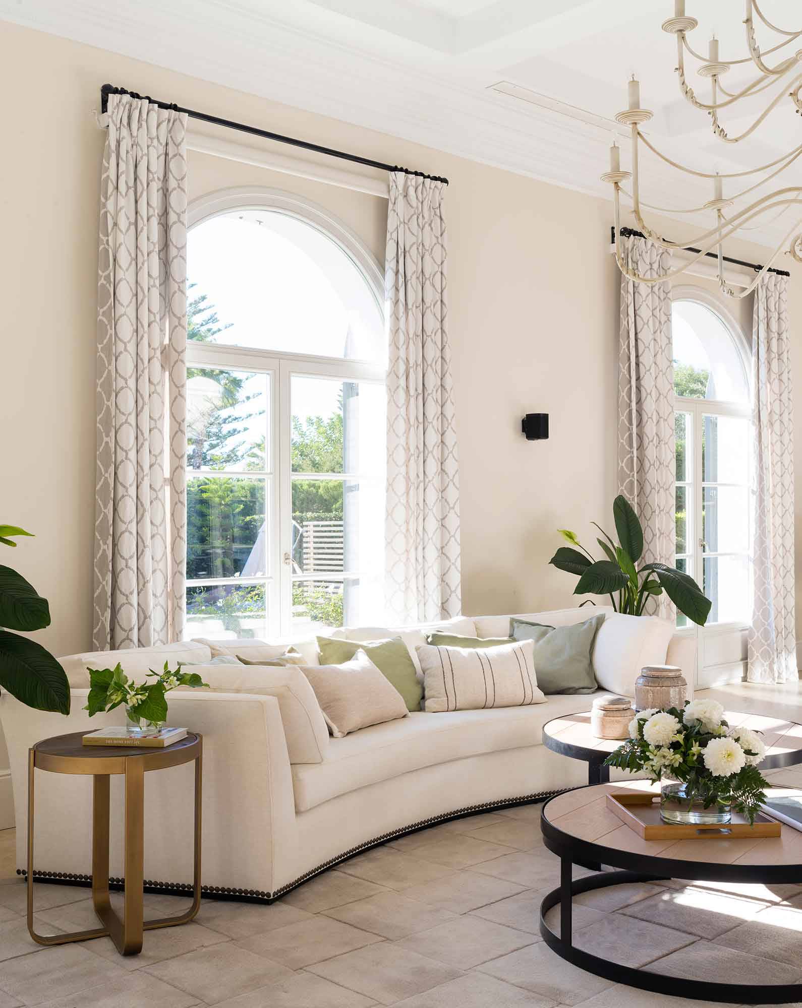 Salón clásico con techos altos, sofá en curva y cortinas estampadas.
