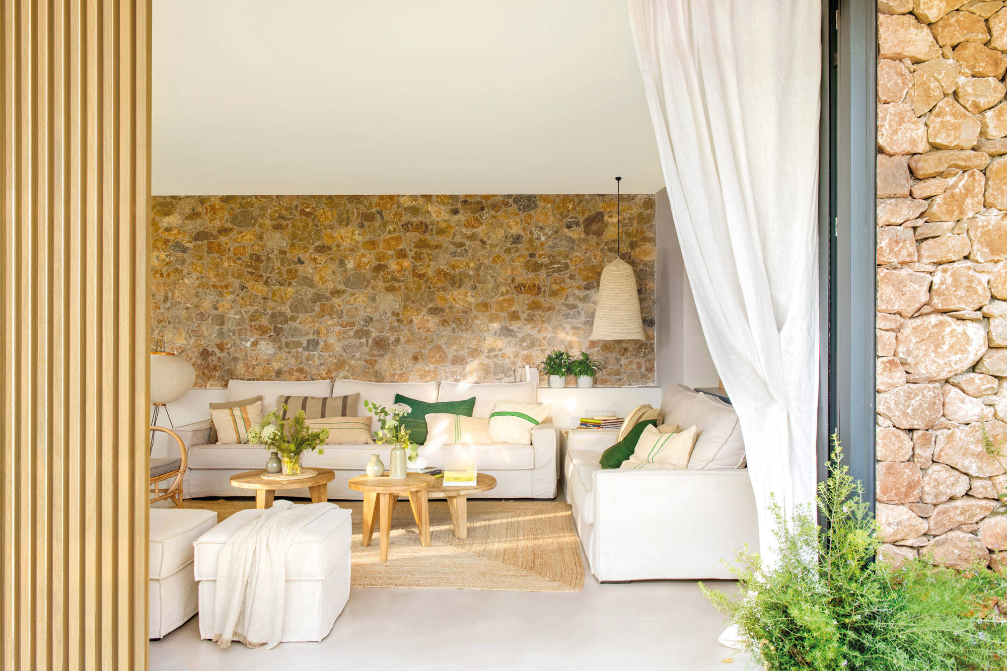 Salón con sofás blancos y pared de piedra.