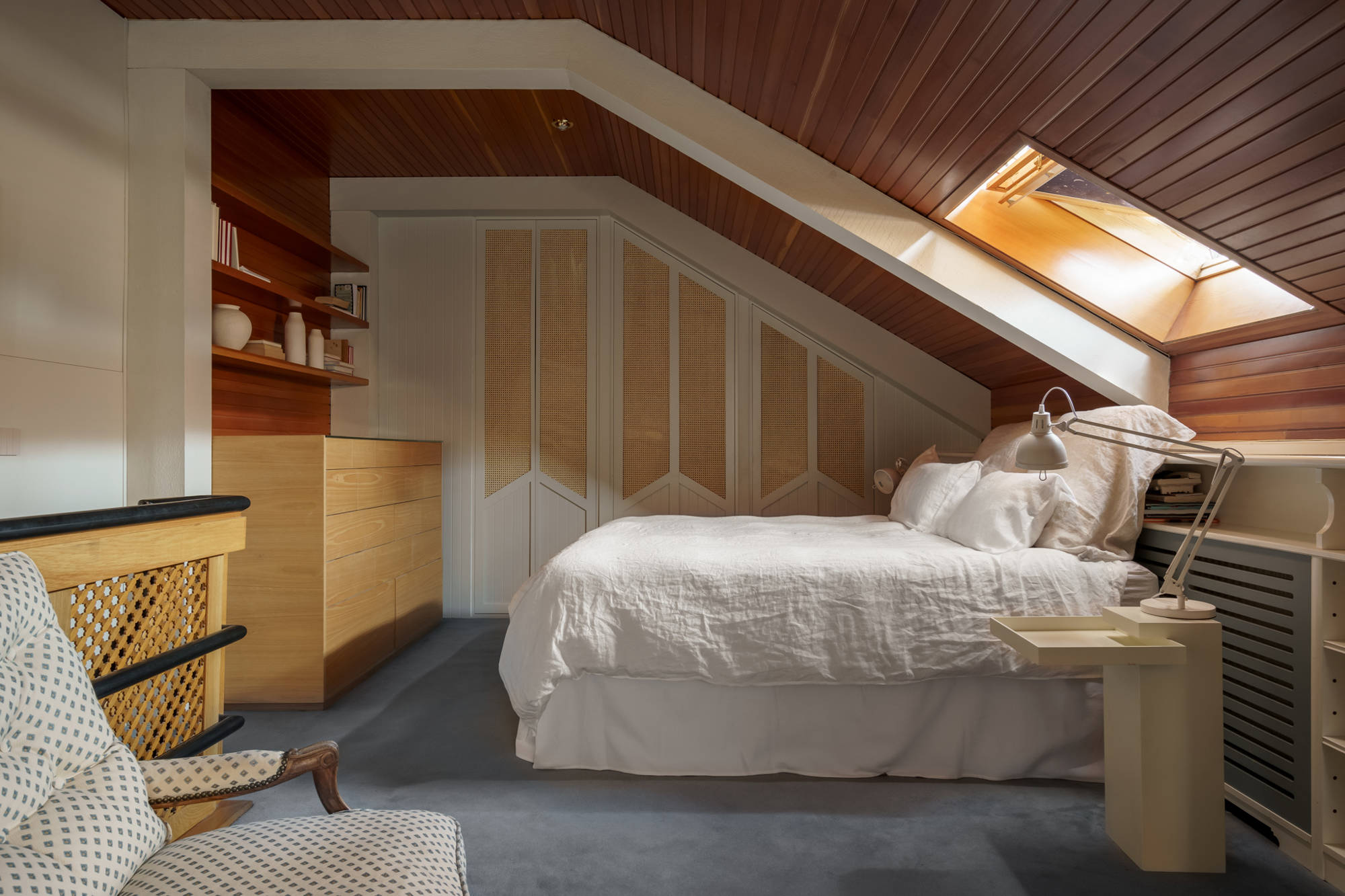 Dormitorio abuhardillado con armario empotrado realizado a medida, moqueta azul y cómoda de madera.