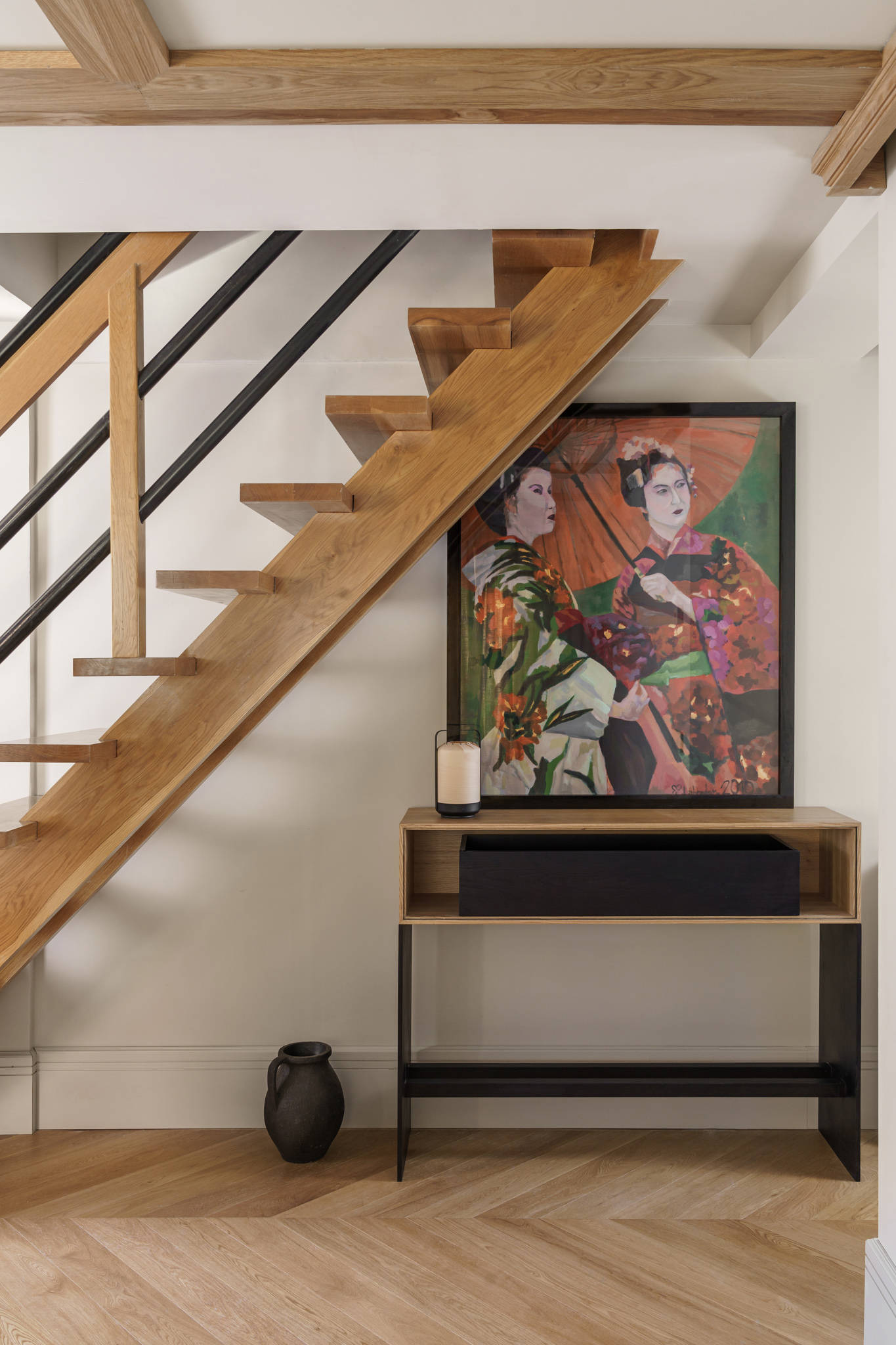 Recibidor con escalera y pavimento de madera, consola, jarrón, vela y cuadro de inspiración asiática.