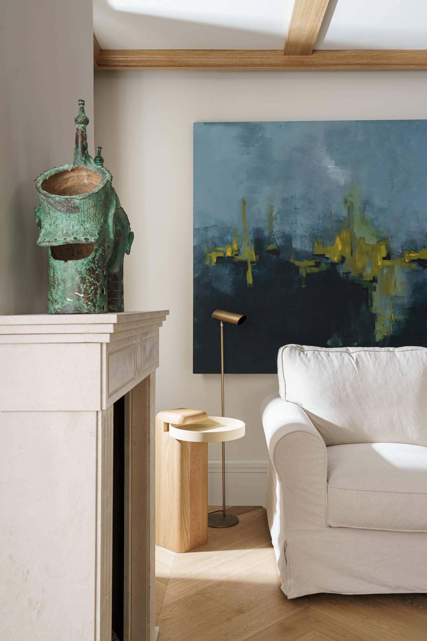 Salón con chimenea de mármol tallada a mano, sofá blanco, mesita auxiliar de madera y cuadro abstracto en la pared.