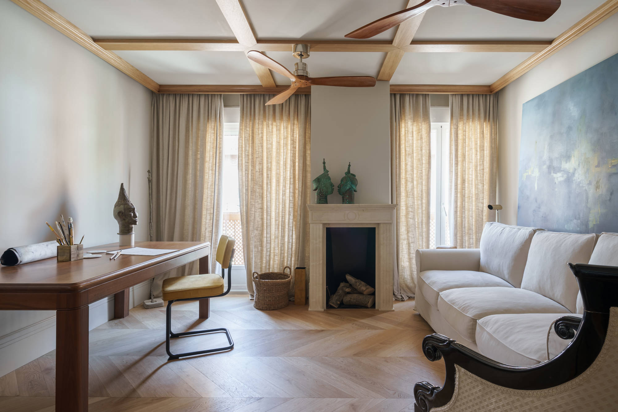 Salón con sofá blanco, ventiladores de madera, chimenea estrecha y escritorio de madera de roble. 