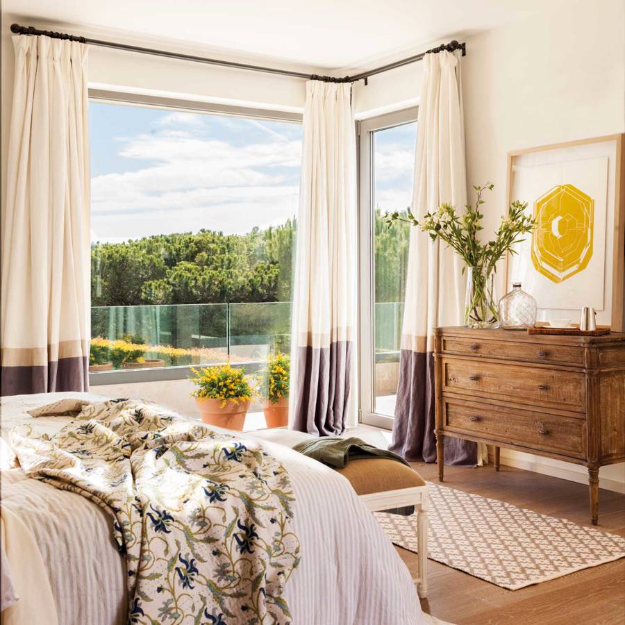 Dormitorio con cómoda a los pies de la cama y cortinas de lino con faldón decorativo