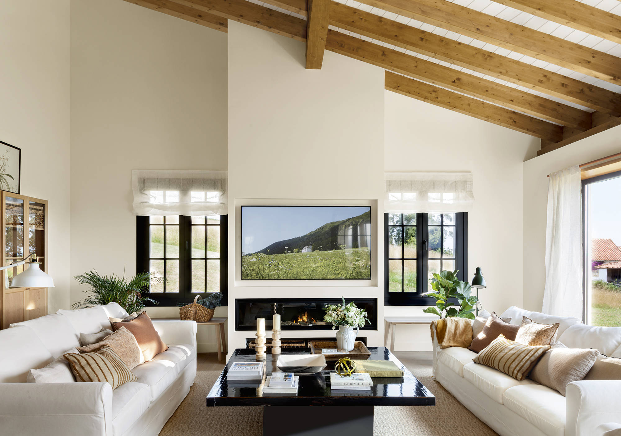 Salón con sofás blancos, mesa de centro negra y chimenea moderna con televisor.