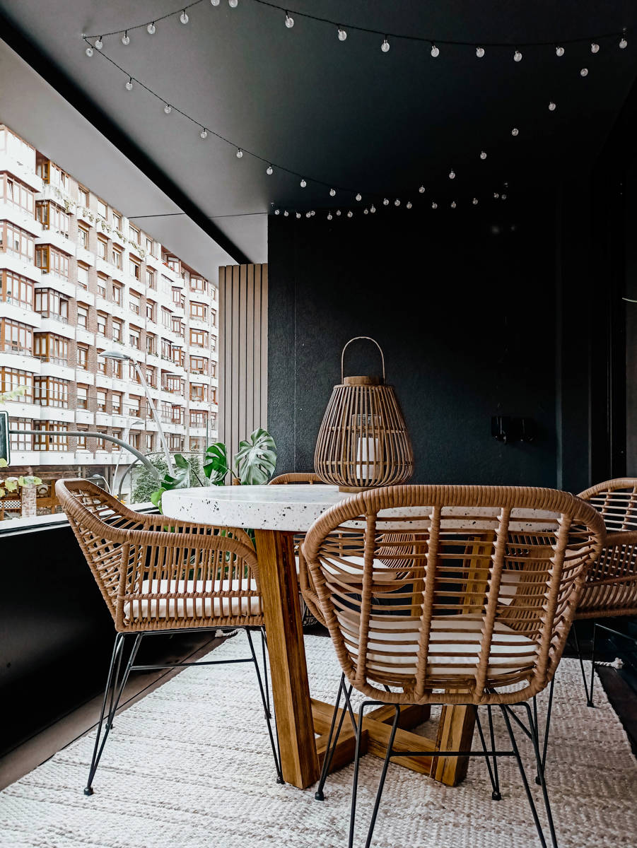 Terraza urbana con mesa de madera y sillas de ratan y hierro negro por Ana Villaman~an