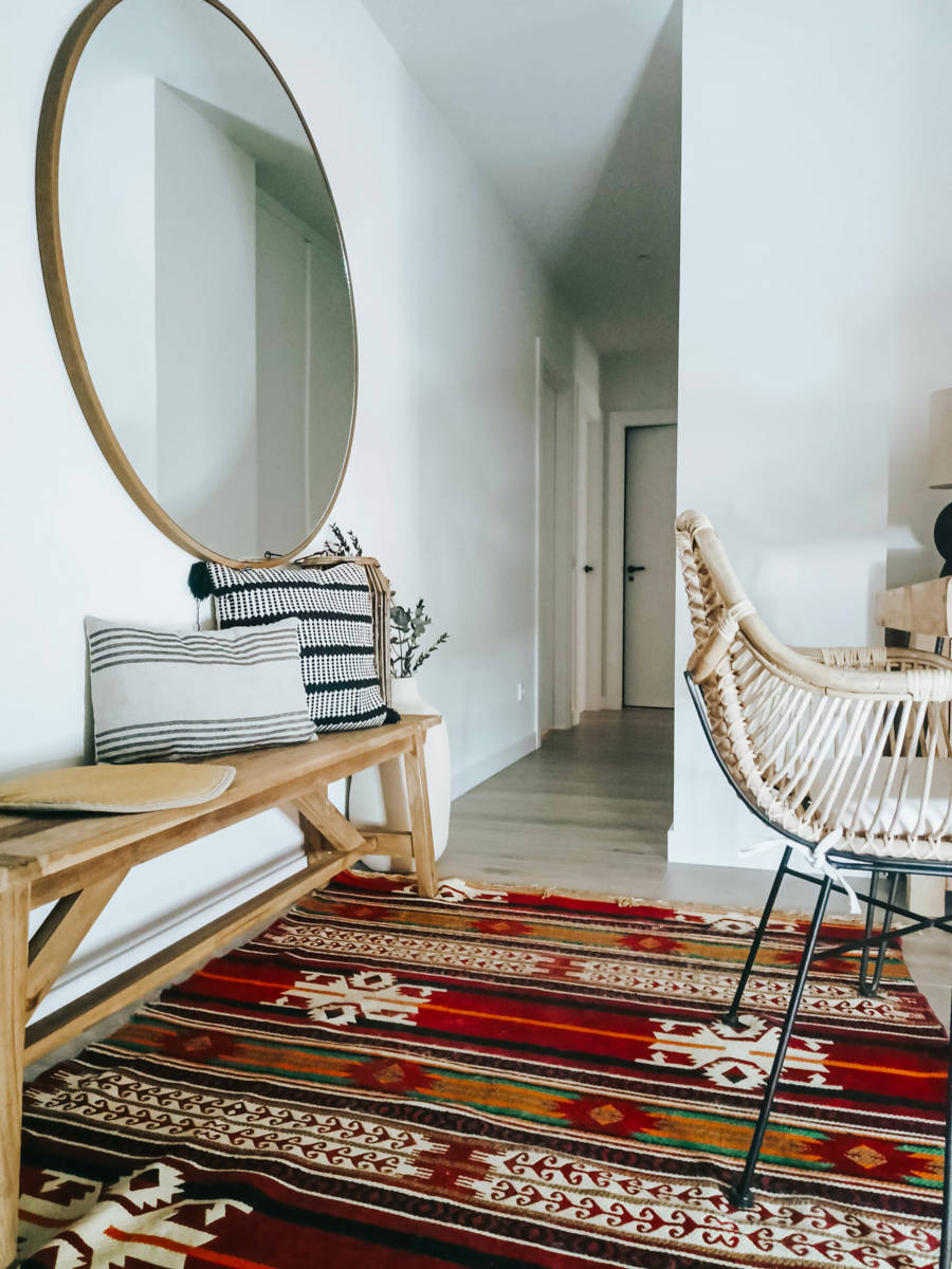 Un pasillo blanco con espejo redondo, banco de madera y alfombra kilim Ana Villaman~an