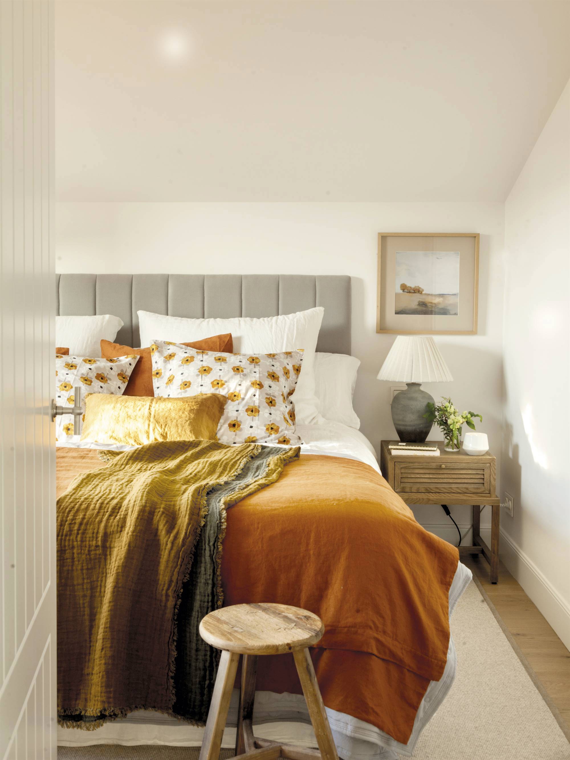 Dormitorio pequeño con cabecero gris y ropa de cama en tonos ocres. 
