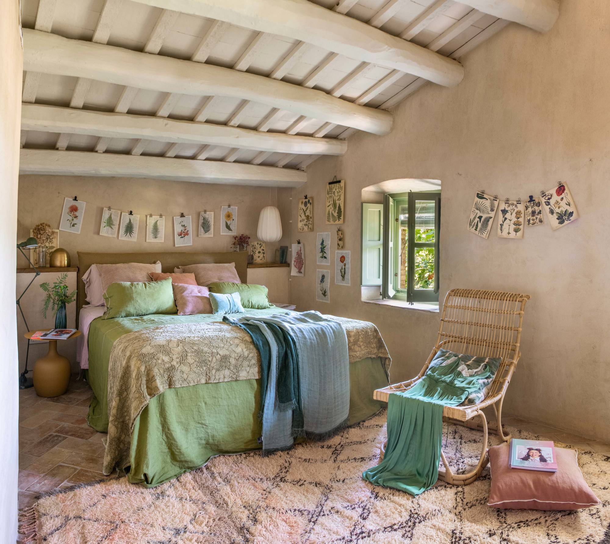 Dormitorio abuhardillado con paredes en tono arena decoradas con láminas botánicas.
