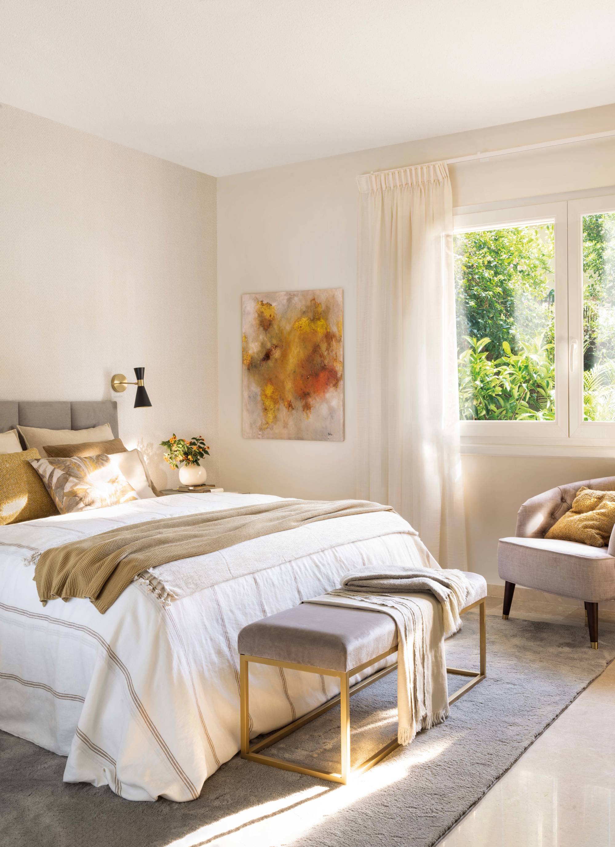 Dormitorio decorados en tonos neutros con butaca y banco a los pies de la cama.