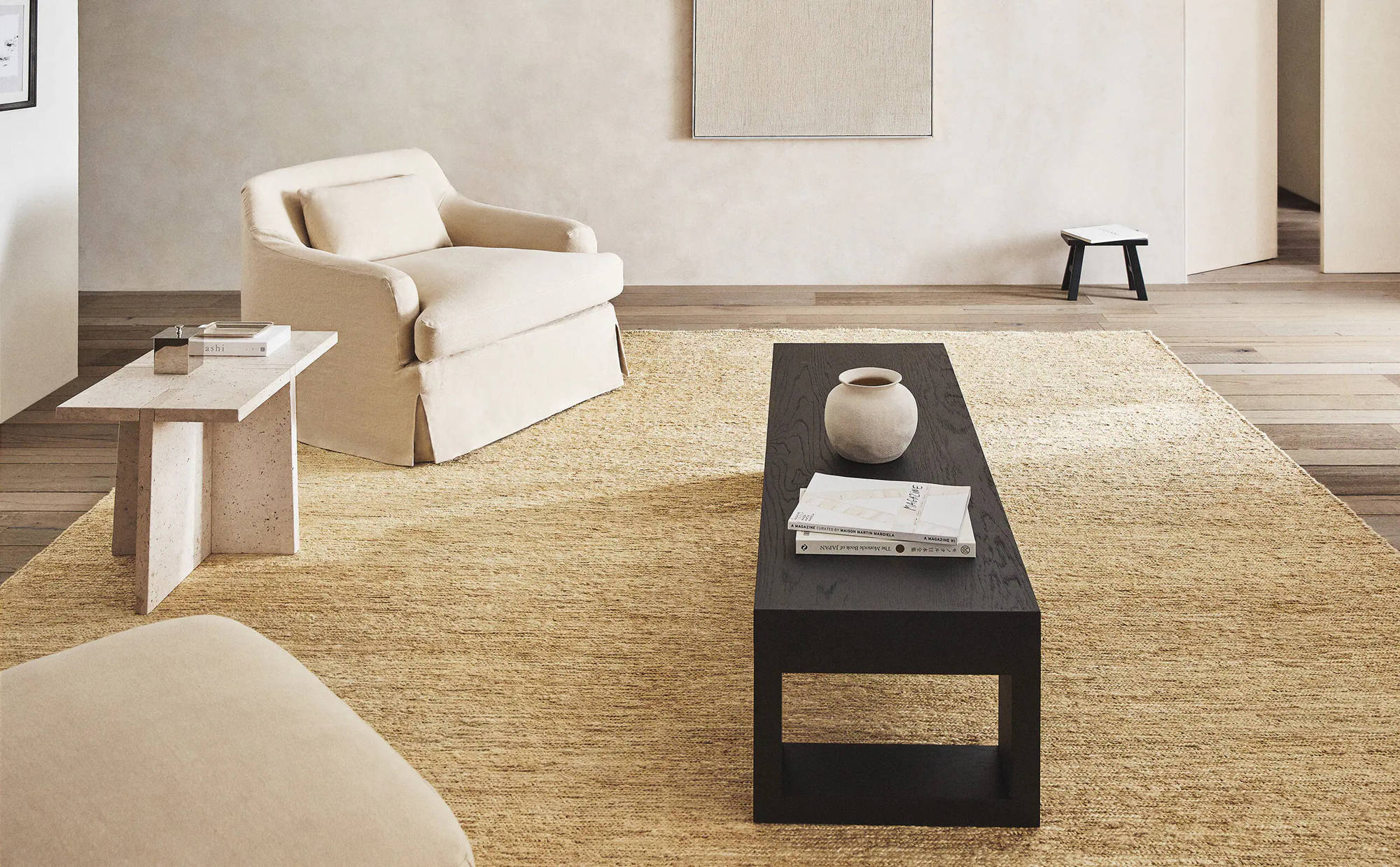 Salón con alfombra XL de yute, mesa de centro oscura y butaca en tonos neutros