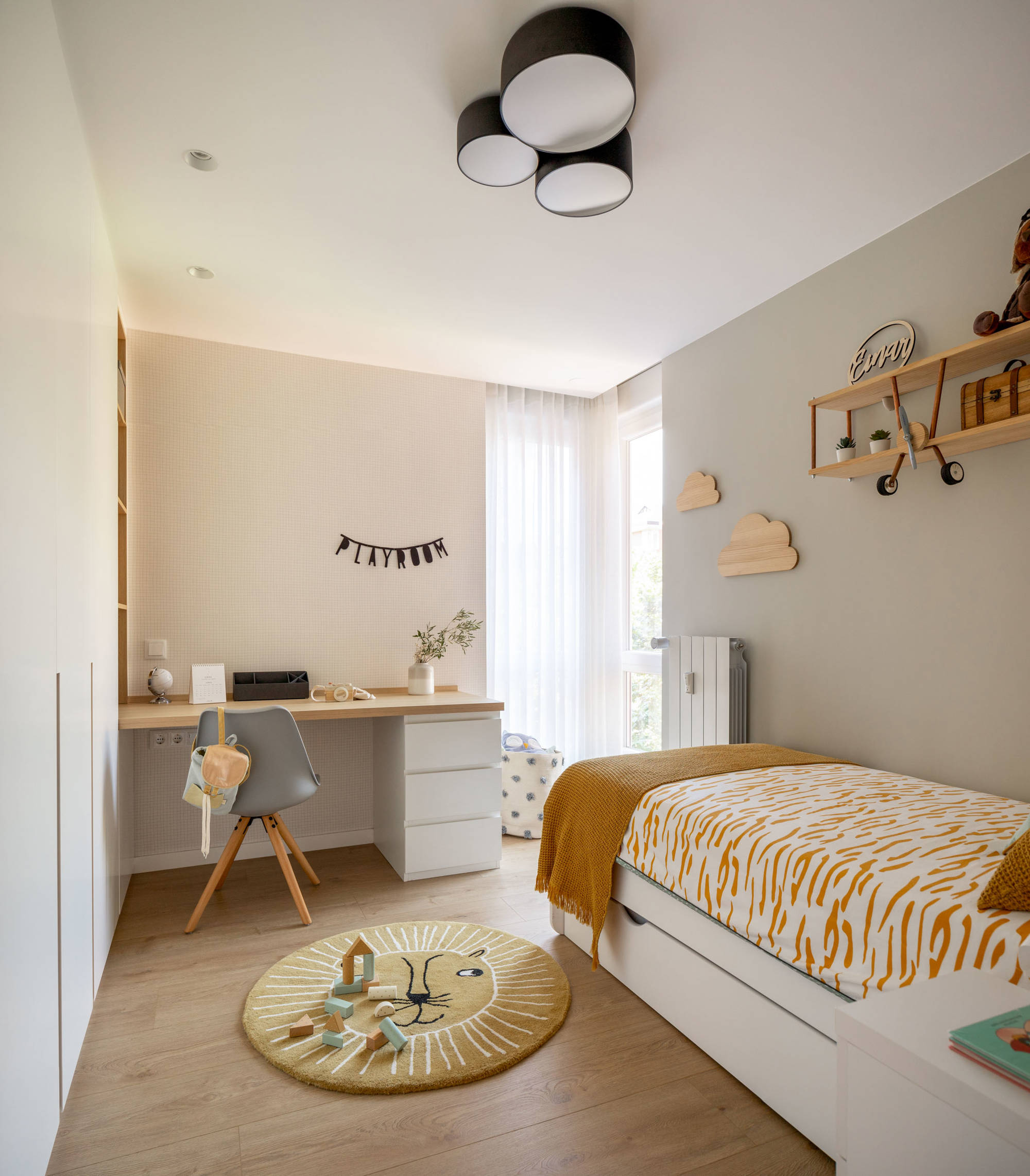 Dormitorio infantil con papel pintada a cuadros, alfombra redonda y mesita auxiliar blanca.
