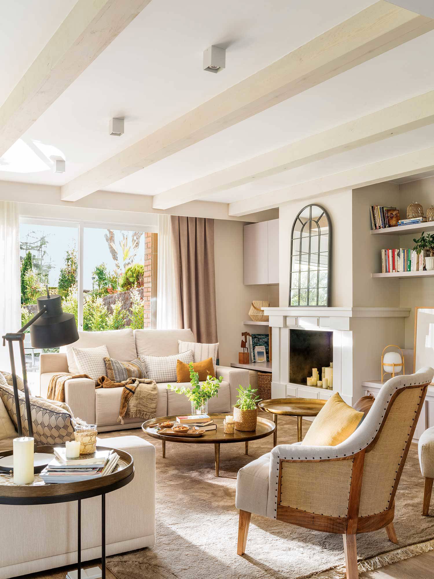 Salón con chimenea, sofás de tela beige y mesas redondas bajas de metal dorado.