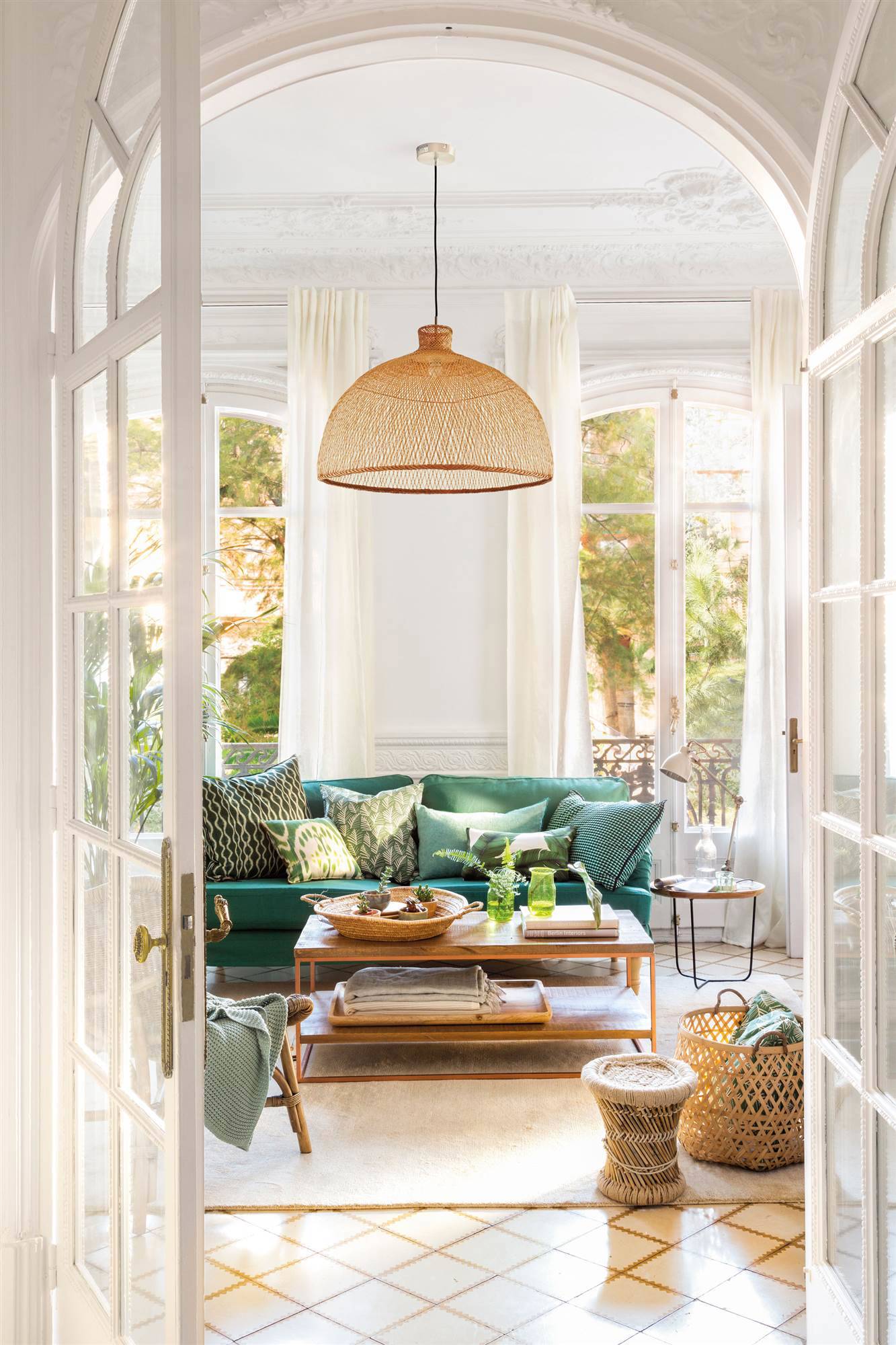 Salón con molduras clásicas, sofá verde, mesa de centro de madera y lámpara de techo con pantalla de fibras.