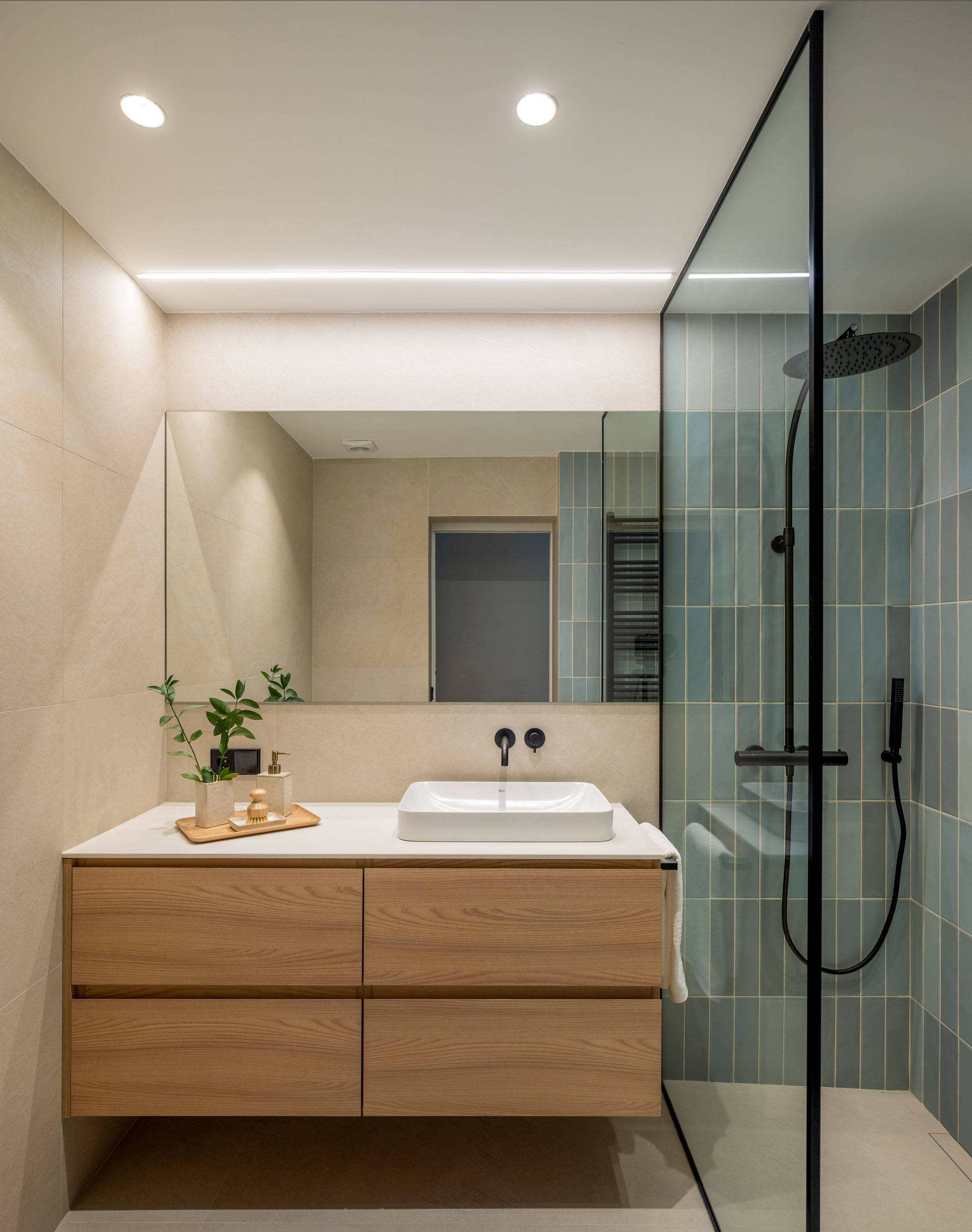 Baño del dormitorio con ducha con revestimiento de azulejos y mueble flotante.